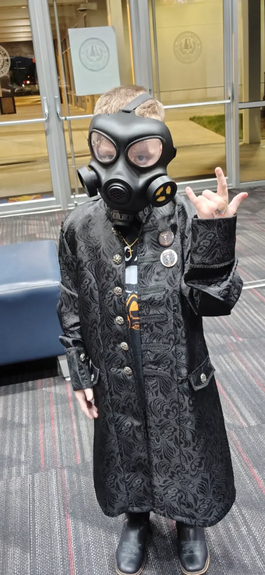 Freak Family member in a gas mask and black coat throwing horns